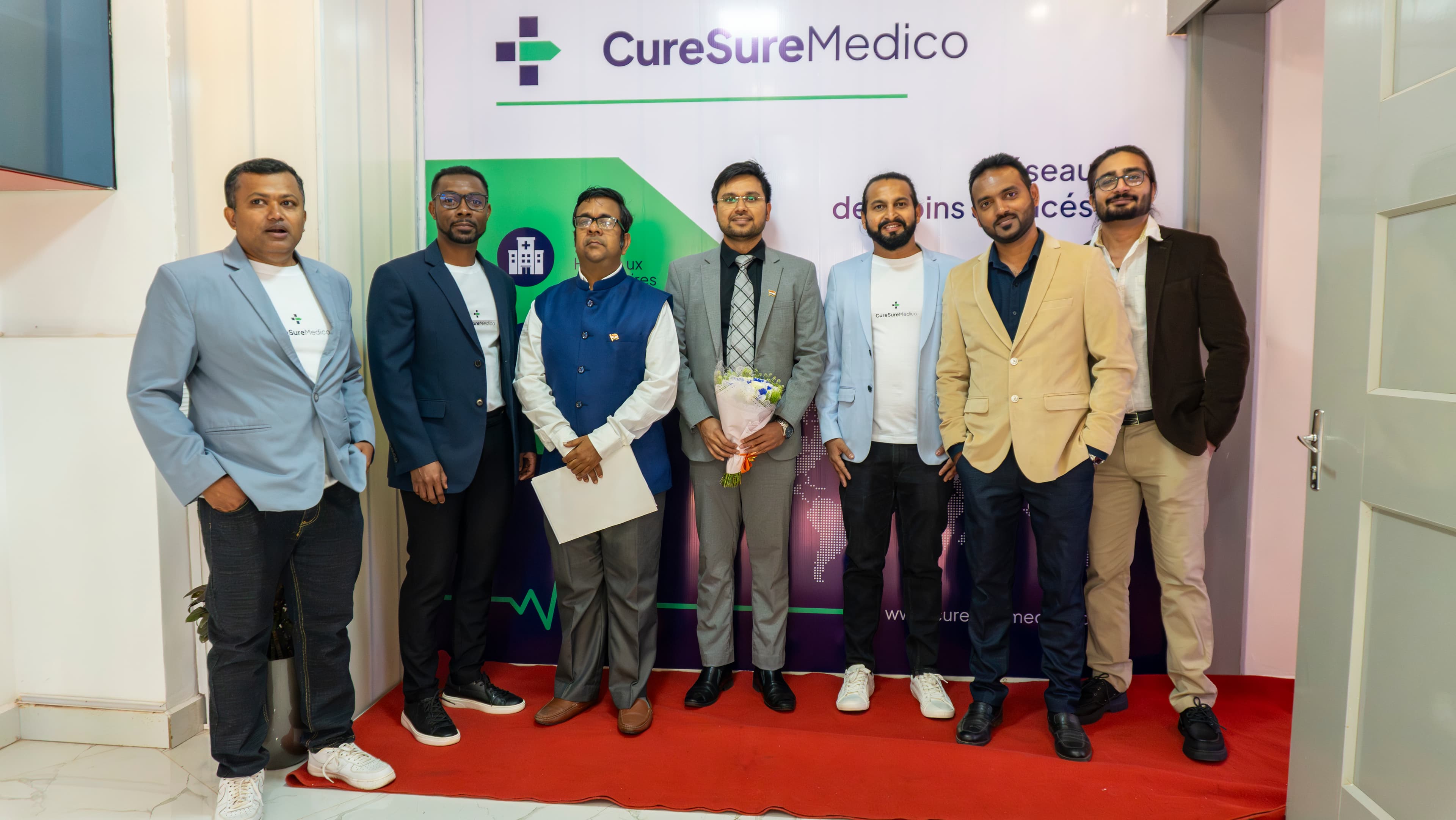 Equipe CureSureMedico devant le mur de marque lors de l'inauguration